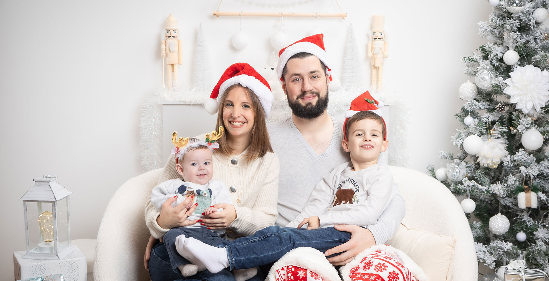 photo d'une mini-séance thème Noël traditionnel en famille avec bonnets rouges assis sur canapé blanc